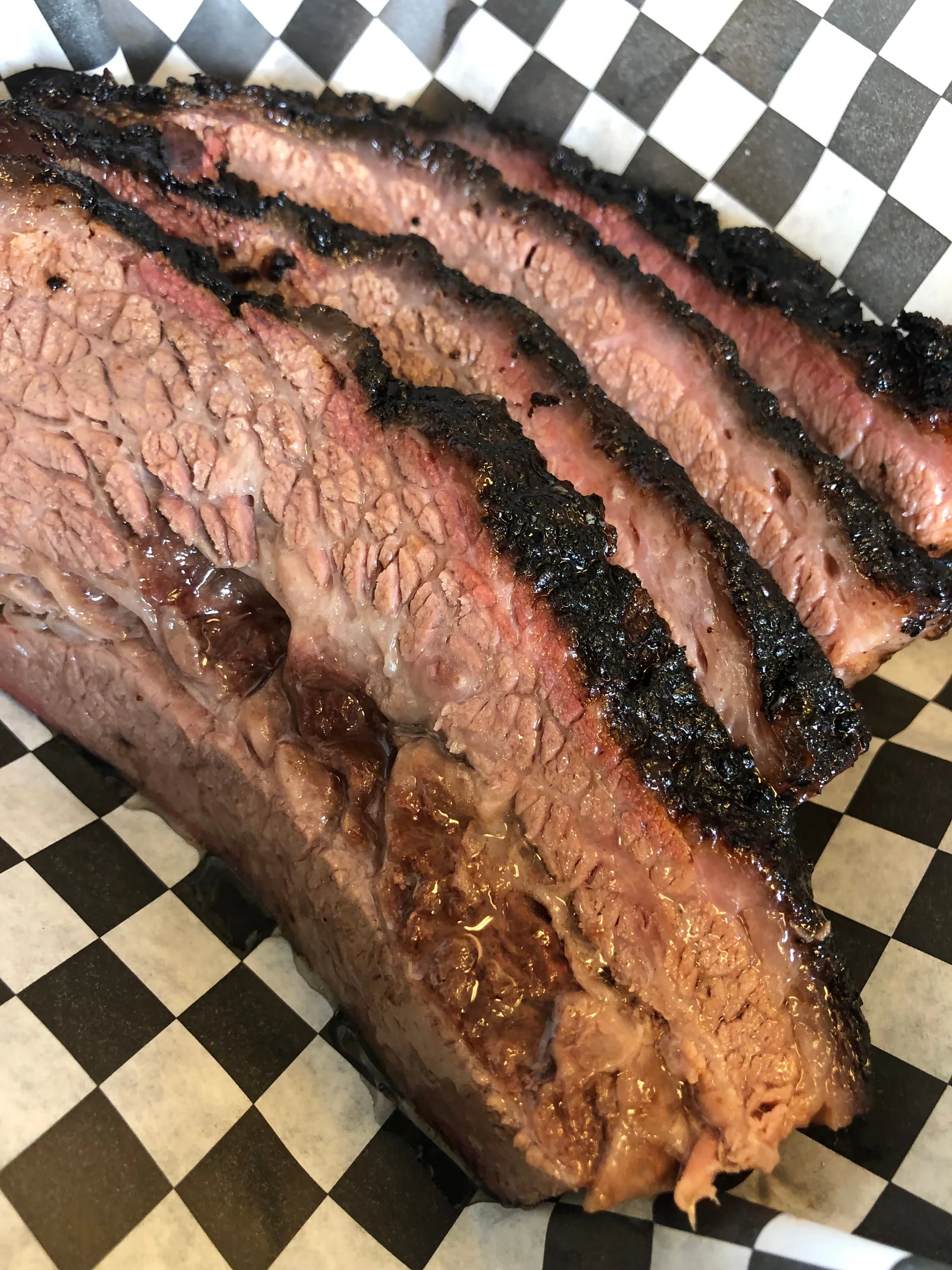 Sliced brisket with dark bark and a pink smoke ring on checkered paper