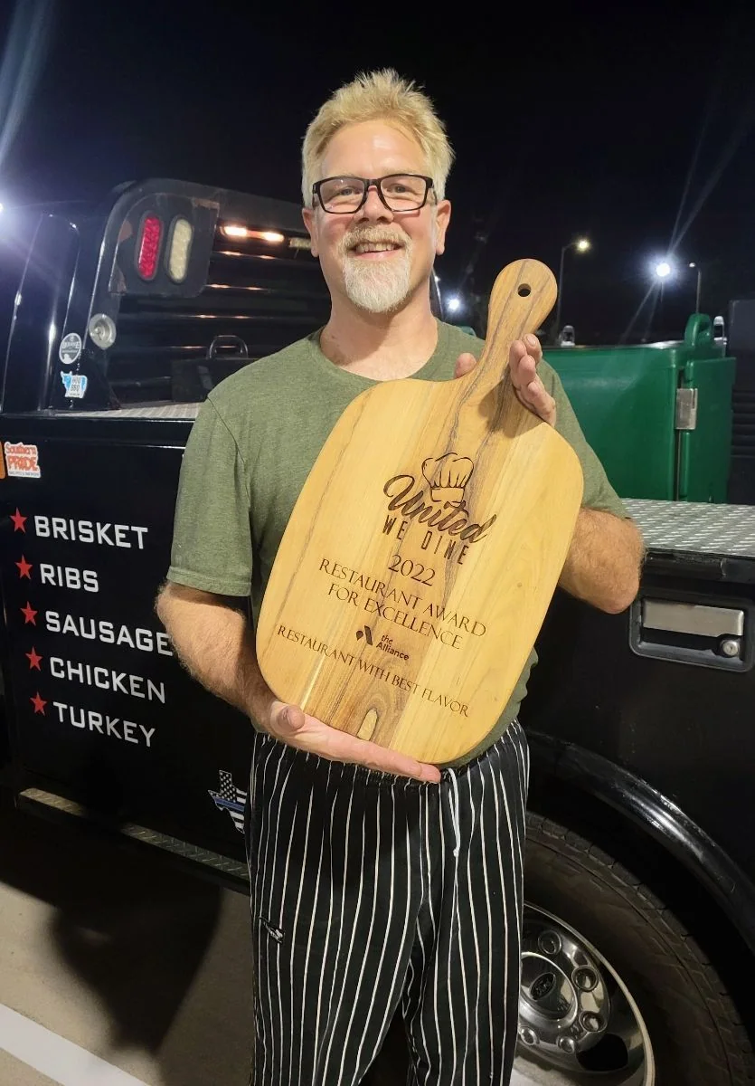 Chef David Welch smiling with a wooden award at an evening event