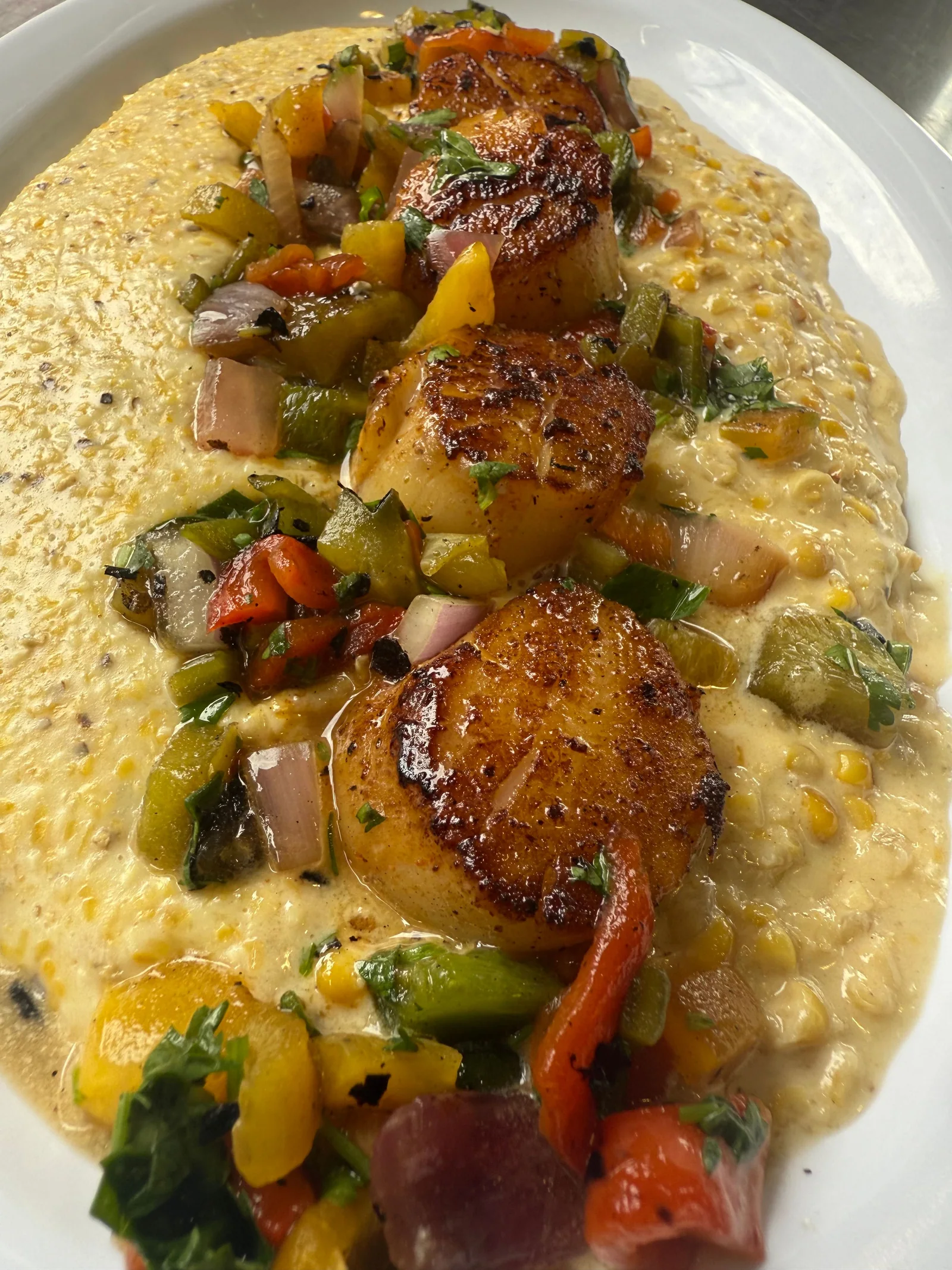 Seared scallops and colorful vegetables arranged on a creamy base