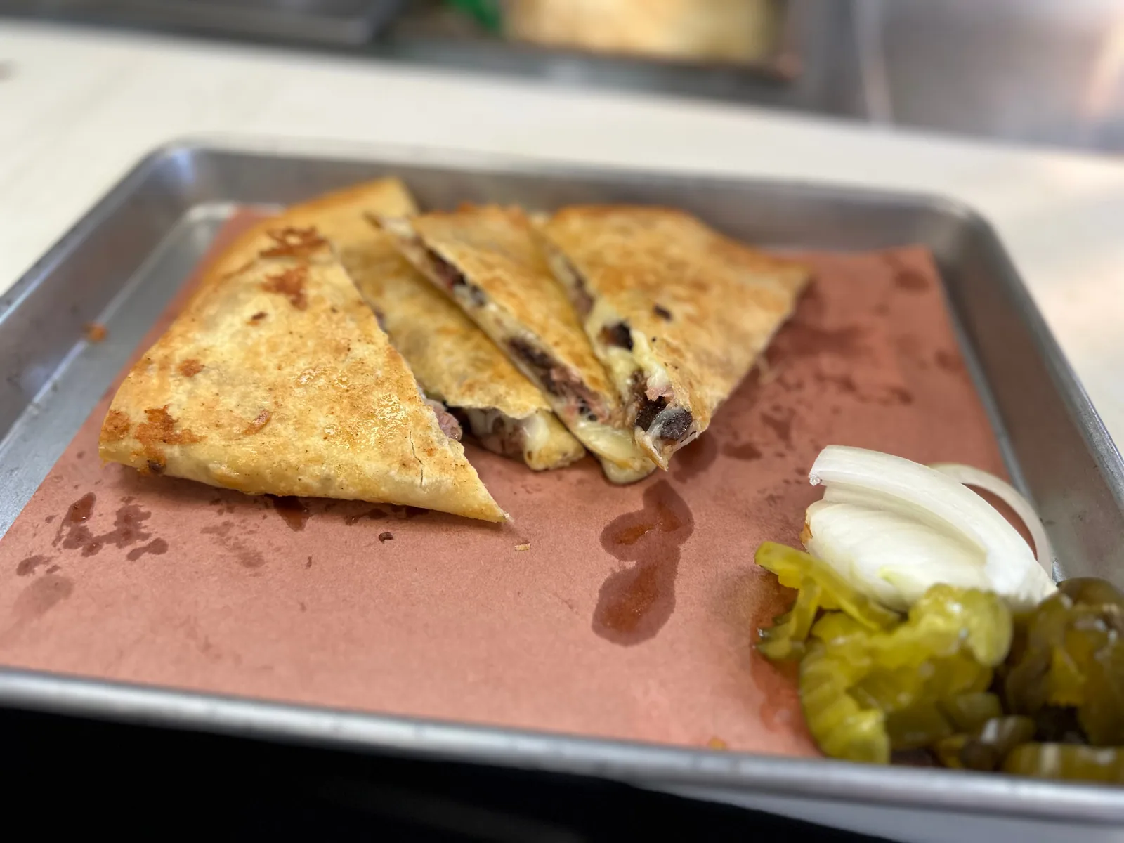 A toasted quesadilla with onions and pickles on a tray