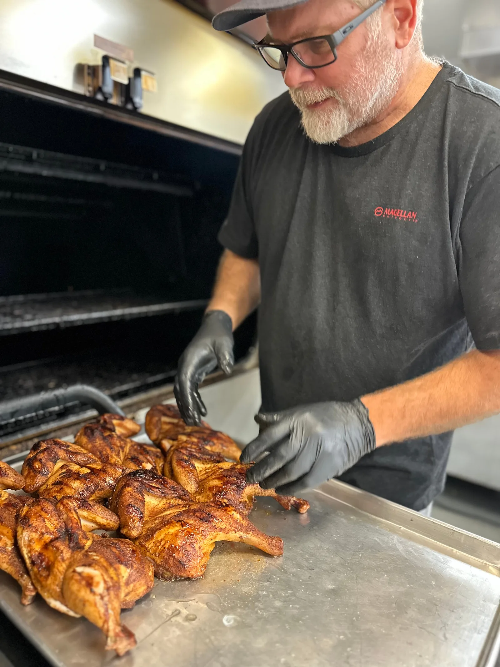 A cook preparing smoked chicken beside the open smoker